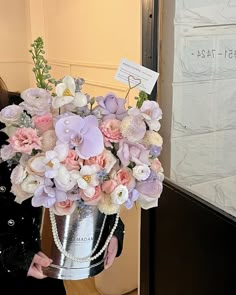 a woman is holding a large silver vase with pink and white flowers in it while standing next to a door