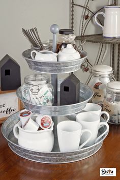 three tiered tray with cups and saucers on it sitting on top of a wooden table