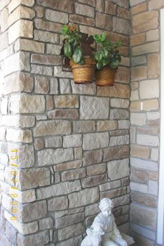 two potted plants sitting on the side of a brick wall next to a statue