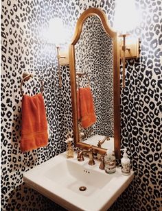 a bathroom with leopard print wallpaper and gold fixtures, two orange towels hanging on the sink