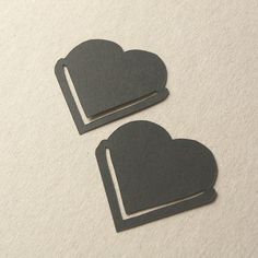 two heart shaped magnets sitting next to each other on a white surface with black paper