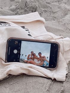 a cell phone sitting on top of a towel next to a pair of feet in the sand