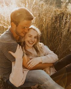 a man and woman sitting on the ground in front of tall grass smiling at each other