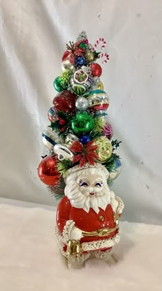 a small christmas tree with ornaments on it's top and santa clause standing next to it