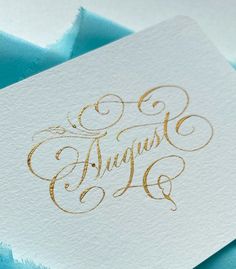 a close up of a piece of paper with gold ink on it and the word august written in cursive writing