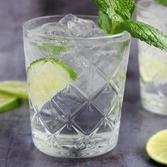 two glasses filled with ice and limes on top of a table next to slices of lime