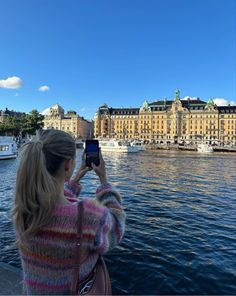 a woman is taking a photo with her cell phone in front of some buildings on the water