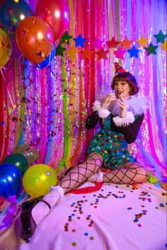 a woman sitting on top of a bed in front of balloons and streamers with confetti