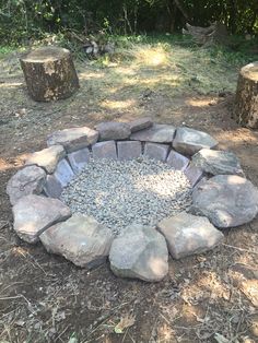 a fire pit made out of rocks in the middle of a field with trees around it