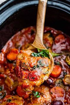 a wooden spoon full of meat and vegetables in a crock pot with tomato sauce