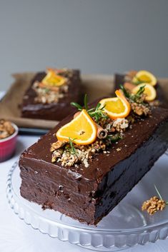 two slices of chocolate cake with oranges and walnuts on top, sitting on a glass platter