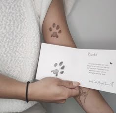 a person holding an open book with a dog paw tattoo on their arm and hand