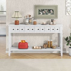 a white console table with lots of items on it and a lamp next to it