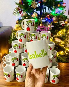 a person holding up a coffee cup with the word salella on it in front of a christmas tree