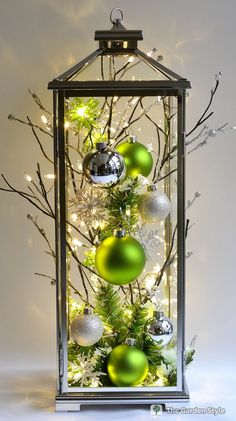 a christmas tree with ornaments and lights in a glass case on a white tablecloth