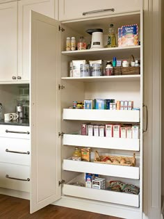 an open pantry door in the middle of a kitchen with white cabinets and wooden floors