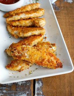 some fried chicken sticks on a white plate with ketchup and dipping sauces