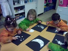 four children are sitting at a table making moon and stars crafts with black paper on them