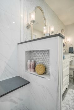 a bathroom with white marble walls and flooring, along with a shelf that has candles on it