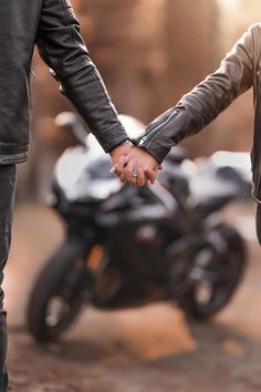 two people holding hands while standing next to a motorcycle