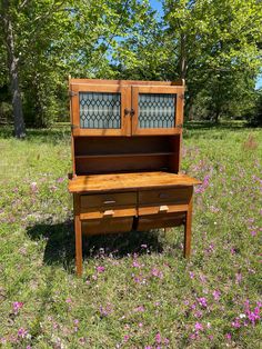 an old wooden desk in the middle of a field with purple flowers and trees behind it