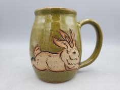 a ceramic mug with a rabbit painted on the front and side, sitting on a white surface