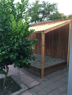 a small wooden structure sitting next to a tree and shrubbery on a brick walkway