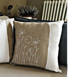 two pillows with embroidered flowers on them sitting on a couch next to a radiator