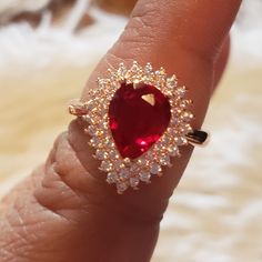 a close up of a person's hand holding a ring with a red stone