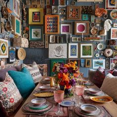 a dining room table with plates and place settings on it in front of a wall full of framed pictures