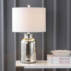 a lamp sitting on top of a white table next to a stack of books and a bowl