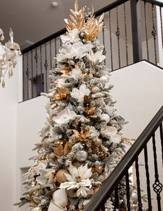 a white christmas tree with gold and silver ornaments on it's branches, in front of a staircase