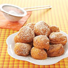 powdered sugar donuts on a white plate with a bowl of dipping sauce in the background