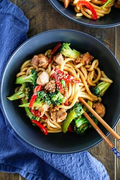 two bowls filled with noodles, broccoli and mushrooms on top of a wooden table