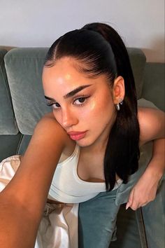 a woman sitting on top of a green couch next to a white wall and holding her hand near her face