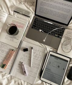 an open laptop computer sitting on top of a bed next to a notebook and pen