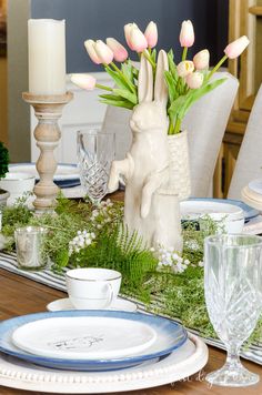 the table is set for easter dinner with flowers and bunny figurines on it