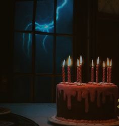 a birthday cake with lit candles sitting in front of a window