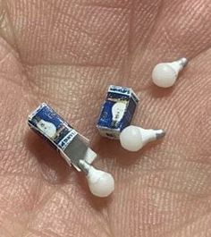 two miniature toothbrushes sitting on the palm of someone's hand, one is white