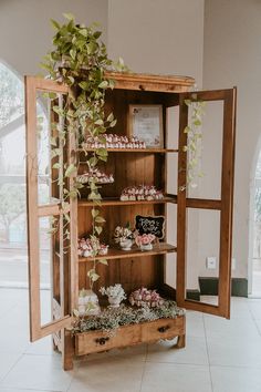 an open bookcase with cupcakes and flowers on it in a room filled with windows