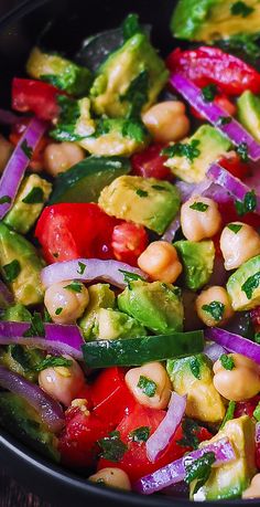 a salad with chickpeas, avocado and red onions in a black bowl