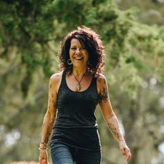 a woman in black shirt and jeans walking on grass with trees in the back ground