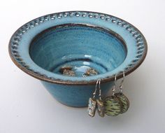 a small blue bowl with silver beads hanging from it's sides and a pair of earrings attached to the side