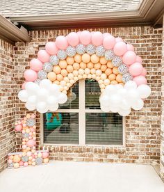 an arch made out of balloons in front of a brick building with a door and window