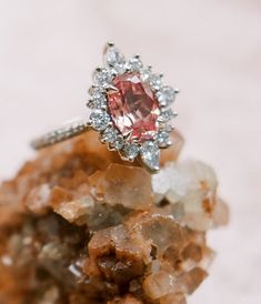 a pink diamond ring sitting on top of a cluster of rocks with crystals around it