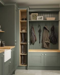 a kitchen with green cupboards and wooden shelves filled with coats, boots and other items