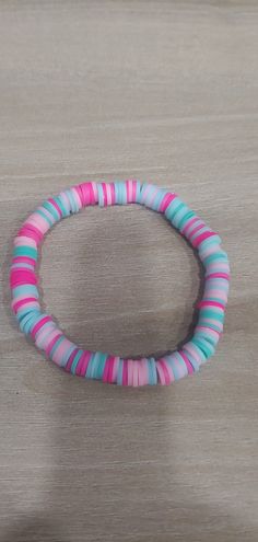 a pink, blue and green bracelet sitting on top of a wooden table