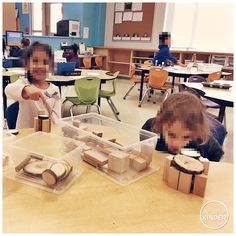 two children are playing with wooden blocks in a class room while another child is pointing at them