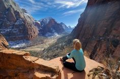 a woman sitting on the edge of a cliff looking at mountains