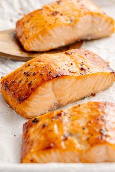 two pieces of cooked salmon on a wooden spoon next to another piece of cooked salmon